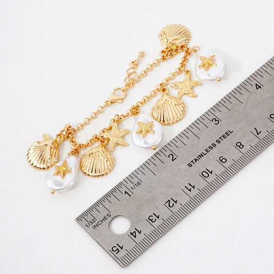 Gold necklace with shell and starfish charms next to a ruler on a white background