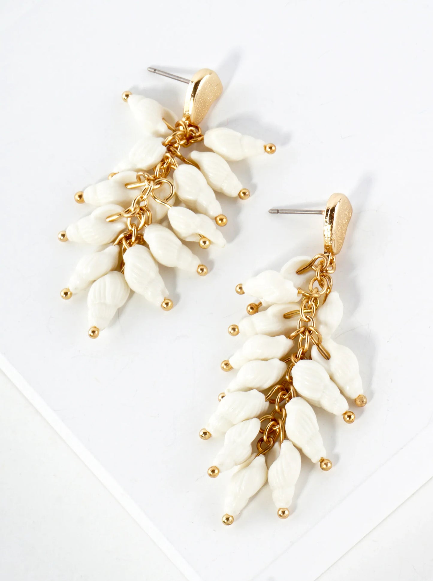 Pair of white leaf-shaped earrings with gold accents on a light gray background